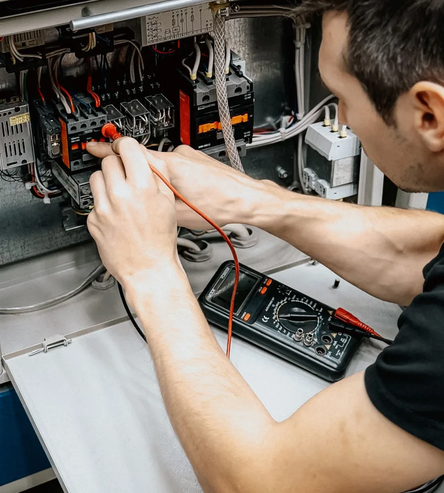 Elektroinstallateur bei der Prüfung eines offenen Sicherungskastens mit Messgerät